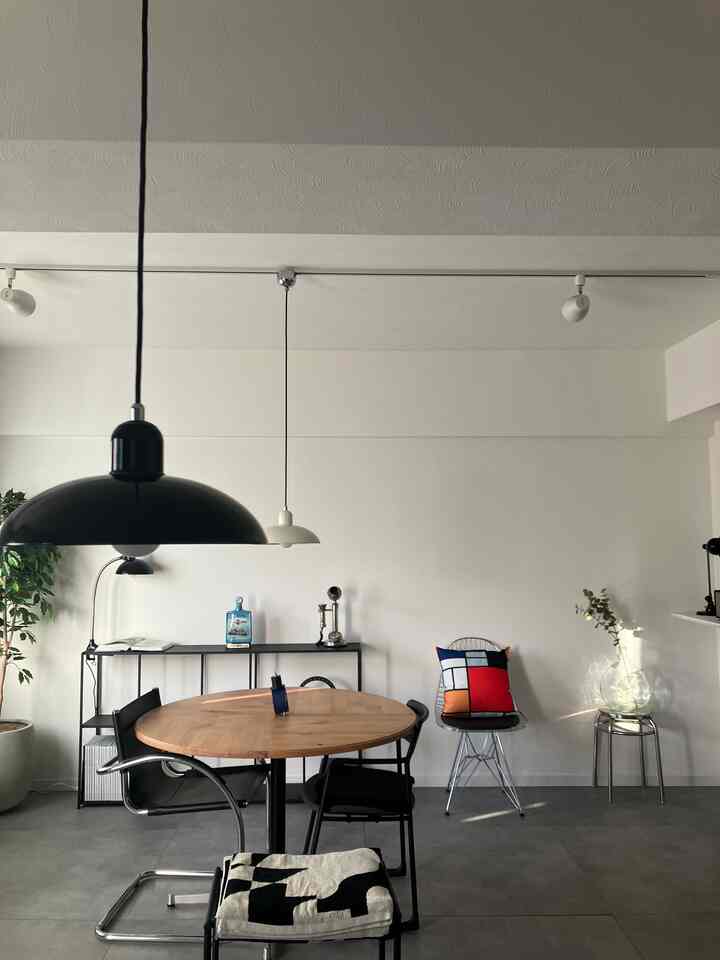 Mid-century modern and industrial living room with white walls and gray floor, featuring a round wood-tone dining table and black pendant lights