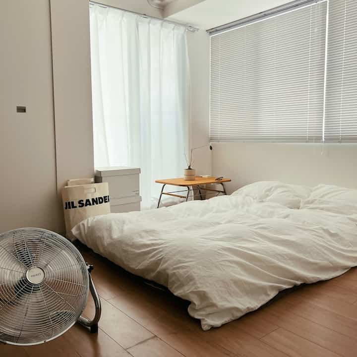 ホワイトとブラウンの色調の寝室、低いベッドとサーキュレーターが配置されたナチュラルモダンな雰囲気のあるインテリア