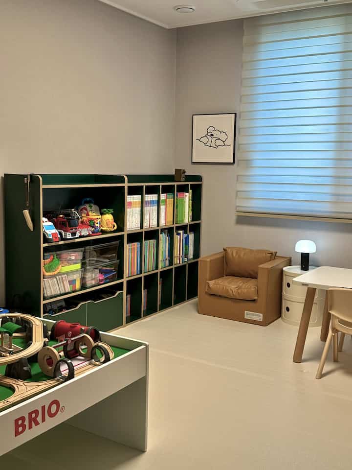 ベージュトーンの床とデスク、オレンジ色のクッション椅子がある子供部屋、整理された多目的本棚とおもちゃが配置された落ち着きのある空間