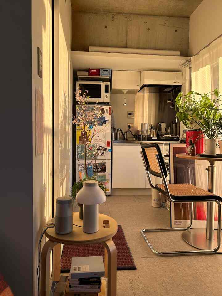 Warm beige-toned studio apartment kitchen and dining area featuring natural material furniture and industrial concrete accents, creating a cozy atmosphere