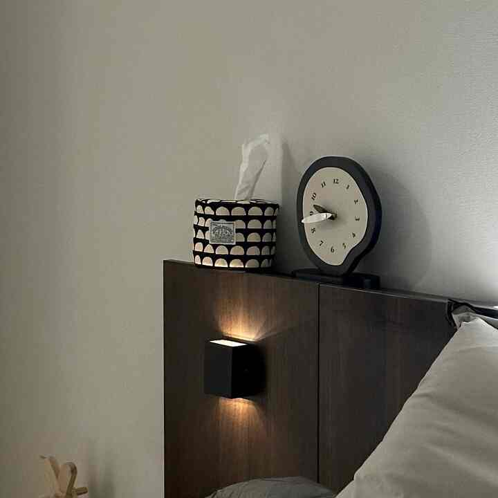 Modern bedroom in black and brown tones featuring a bed headboard with clock and half-moon tissue cover creating a cozy atmosphere