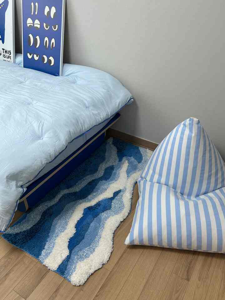 青と白の調和が取れた寝室、青いベッドカバーと波模様のラグ、ストライプのビーズクッションが配置された雰囲気のあるインテリア