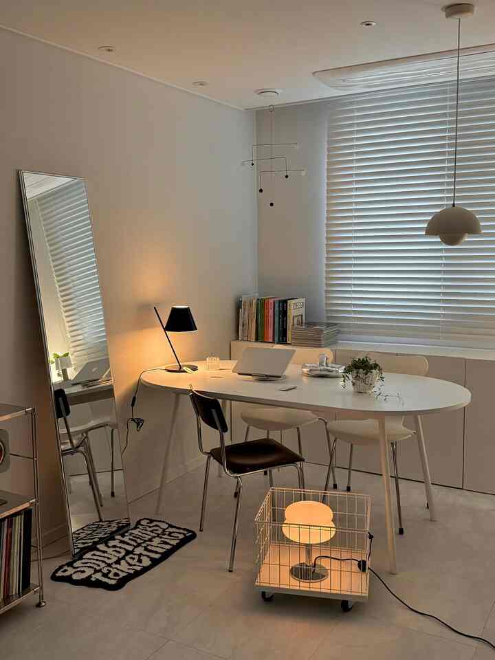 白を基調としたダイニング兼書斎、白い楕円形のテーブルと椅子、全身鏡やブラインドが配置されたシンプルで落ち着いた空間