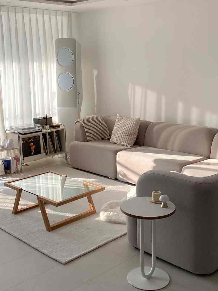 ナチュラルカラーのリビング、大きなベージュのソファとガラスのコーヒーテーブルが配置された、落ち着いた暖かみのある空間