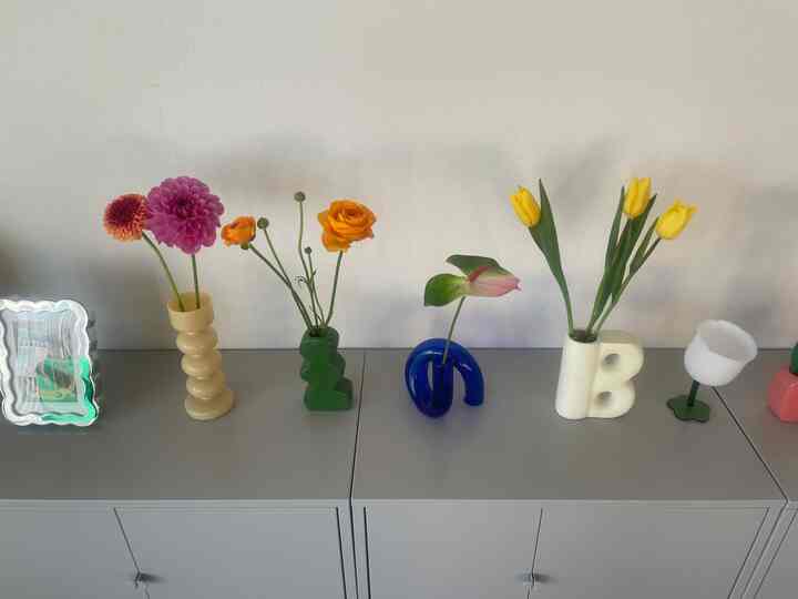 グレーのチェストの上にさまざまなカラフルな花瓶と花が並んだシンプルでモダンなインテリアの空間