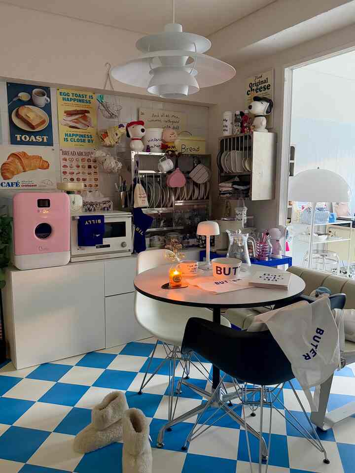 White and blue tiled kitchen featuring a round dining table with assorted chairs, styled in a cozy cafe-inspired atmosphere