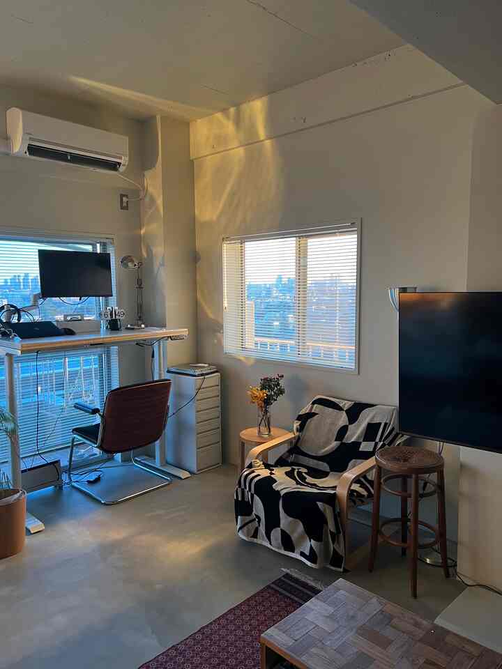 ベージュの壁と木目調の家具が配置されたモダンなリビング兼ホームオフィス空間、夕日の暖かい光が差し込む雰囲気のあるインテリア