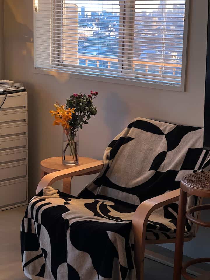 Living room with natural wood tones and white walls, featuring an armchair draped with a black and white patterned throw creating a cozy atmosphere