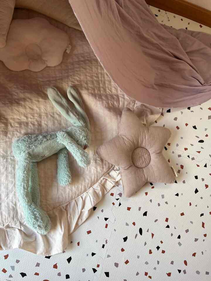 ピンクとベージュの色調の子供部屋、赤ちゃん用寝具やクッション、パターンマットが配置された雰囲気のあるインテリア