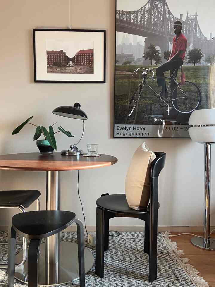 Natural-colored dining room featuring round dining table, black dining chairs, table lamp, and plant in a modern setting