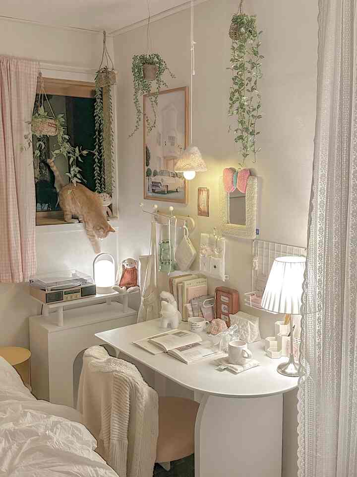 白とナチュラルな色調のワンルーム書斎、机と吊るされた植物が配置され、窓辺で猫が遊んでいる落ち着いた空間。