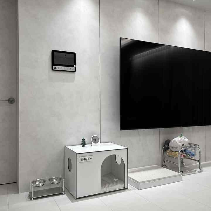 明るいホワイトトーンのリビングルーム、壁掛けテレビとペットハウス、ステンレス製バスケットトロリーカートが配置された整然とした空間