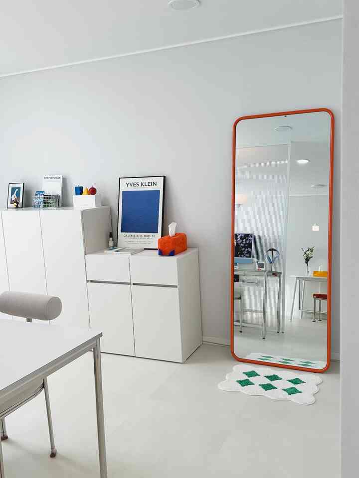 白とオレンジの色調が調和したミッドセンチュリーモダン風のすっきりとした空間、大きなオレンジフレームの鏡とポスターが配置された印象的なインテリア