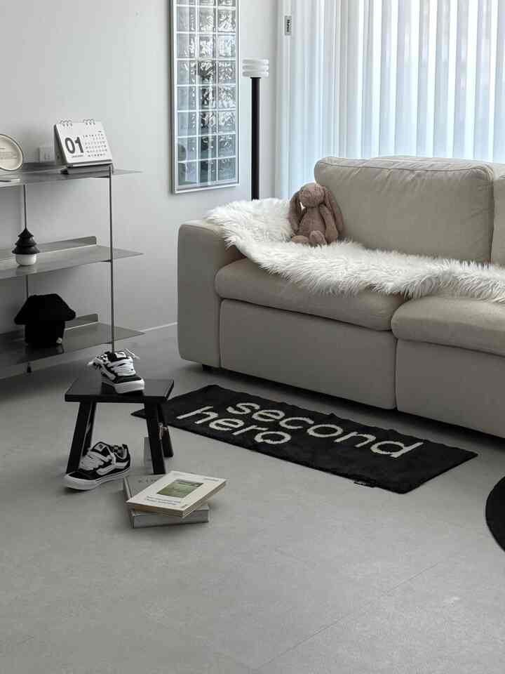 白とベージュの色調のリビング、ベージュのソファと白いファー飾り、黒いスツールとラグが配置されたモダンでミニマルな雰囲気のインテリア