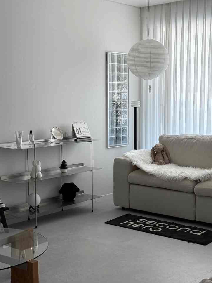 白とベージュのトーンのモダンでナチュラルなリビング、ベージュのソファとメタルシェルフ、丸いペンダントライトが配置された印象的な空間