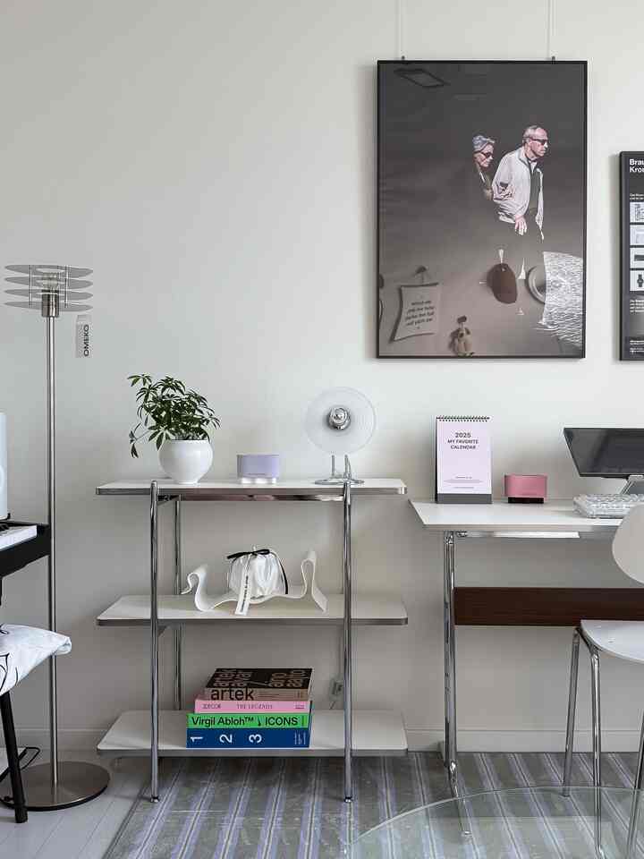 白とグレーのトーンでまとめられたミニマルなリビングルーム、棚、デスク、フロアランプ、ポスターが配置された空間