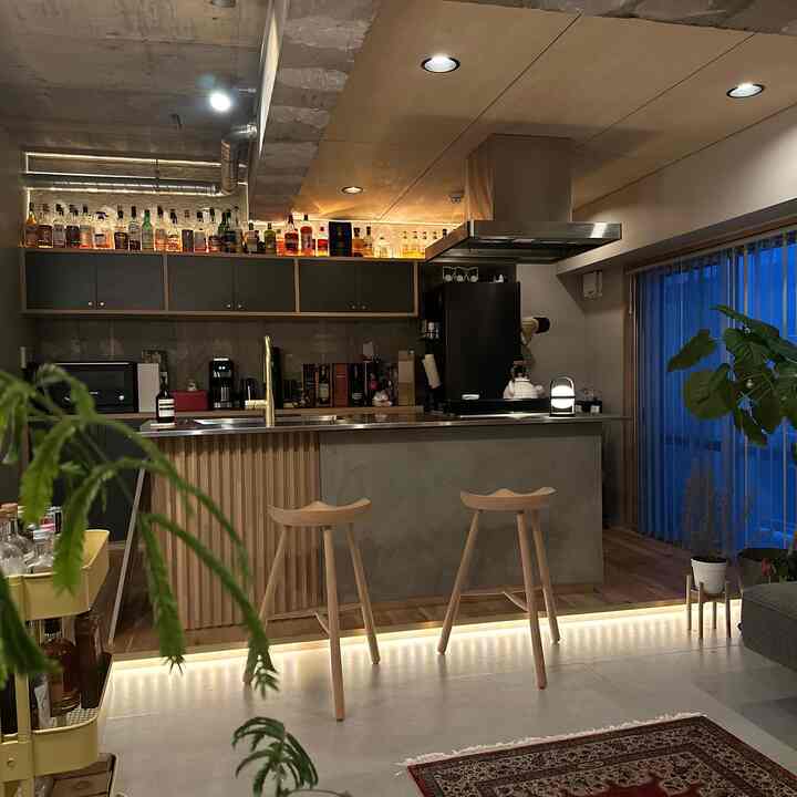 グレーと木目調が調和したモダンなキッチンスペース、ホームバーやバースツール、植物が配置されて落ち着いた雰囲気のインテリア