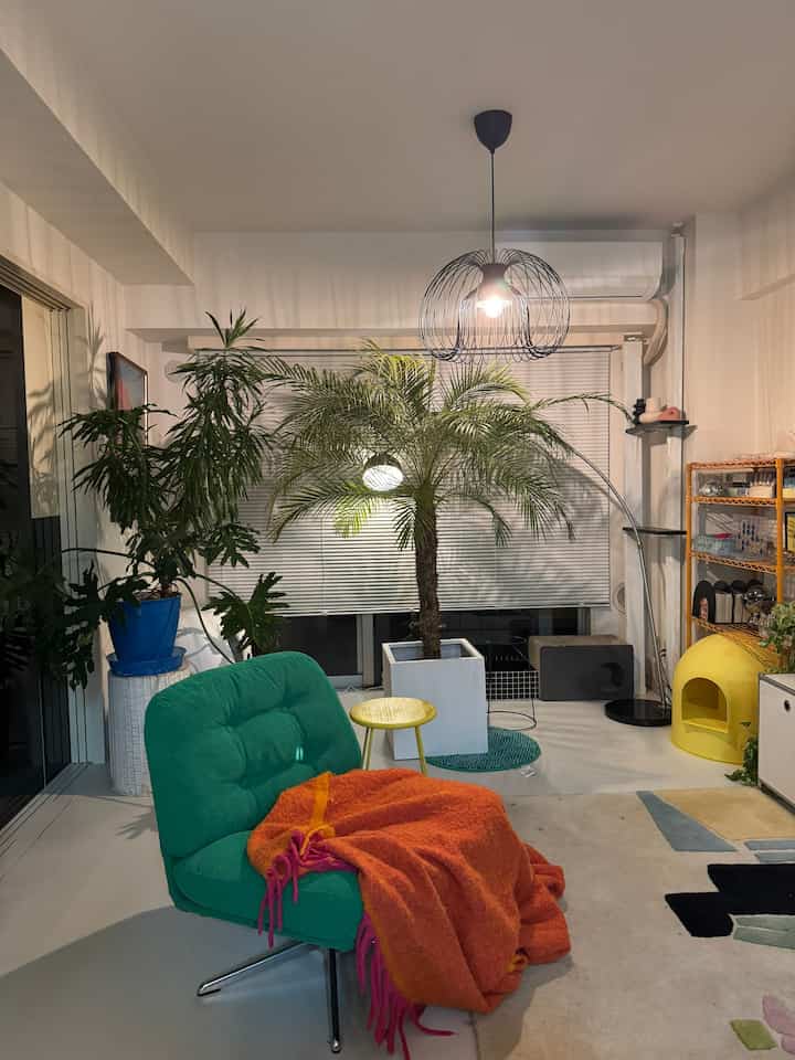 White-walled living room with a large central palm plant, green armchair, and yellow cat house creating a cozy natural style ambiance