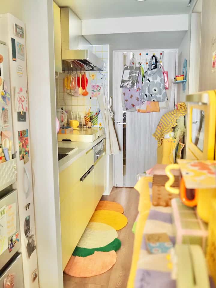 Bright yellow-toned narrow kitchen space featuring colorful utensils and a multicolored rug, creating a cozy interior