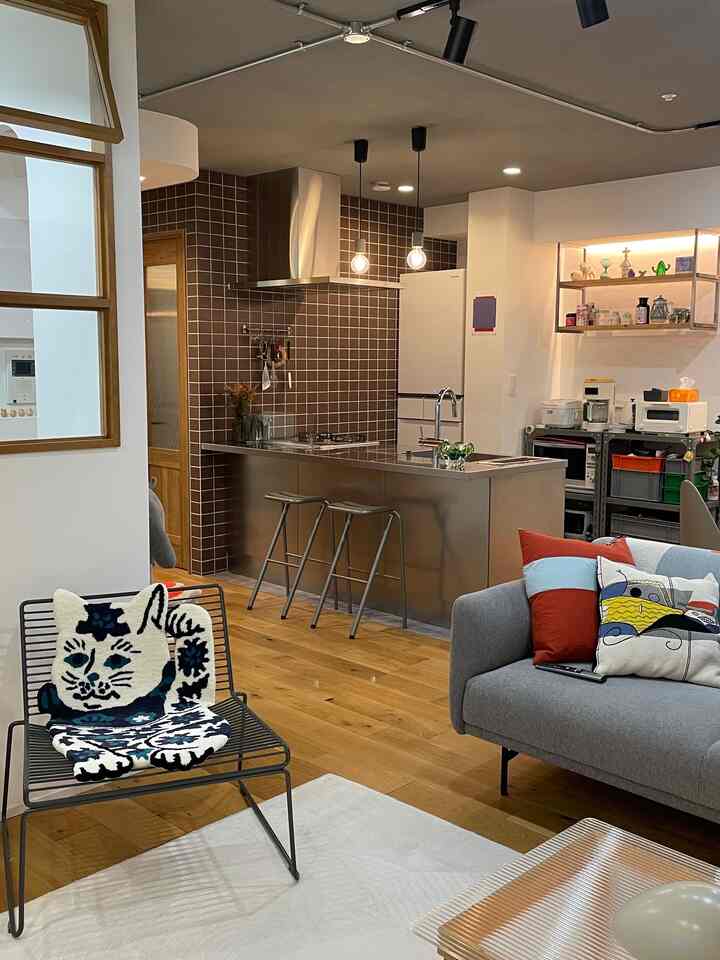 ナチュラルカラーの木製フローリングとモダンなステンレス製キッチンアイランド、グレーのソファとアームチェアが配置された印象的なリビング空間