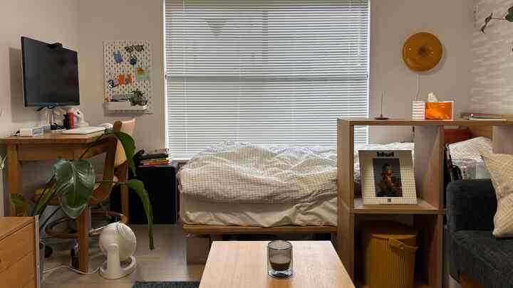 白とナチュラルウッド調の7畳ワンルーム寝室、デスクが配置されたシンプルで居心地の良い一人暮らしの空間