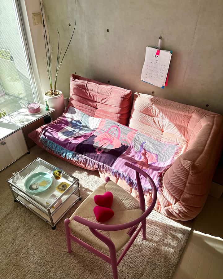 ピンク色のソファとカーペットがある自然光のリビング、カラフルなブランケットとCH24 Yチェアが配置された雰囲気のある空間
