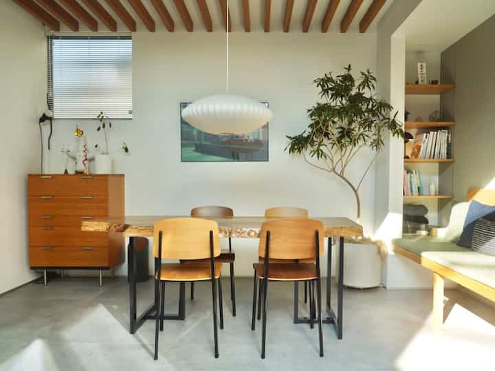 白い壁と木目調の家具が調和する明るいダイニング、食卓と椅子、ペンダントライトが配置された自然な雰囲気のインテリア