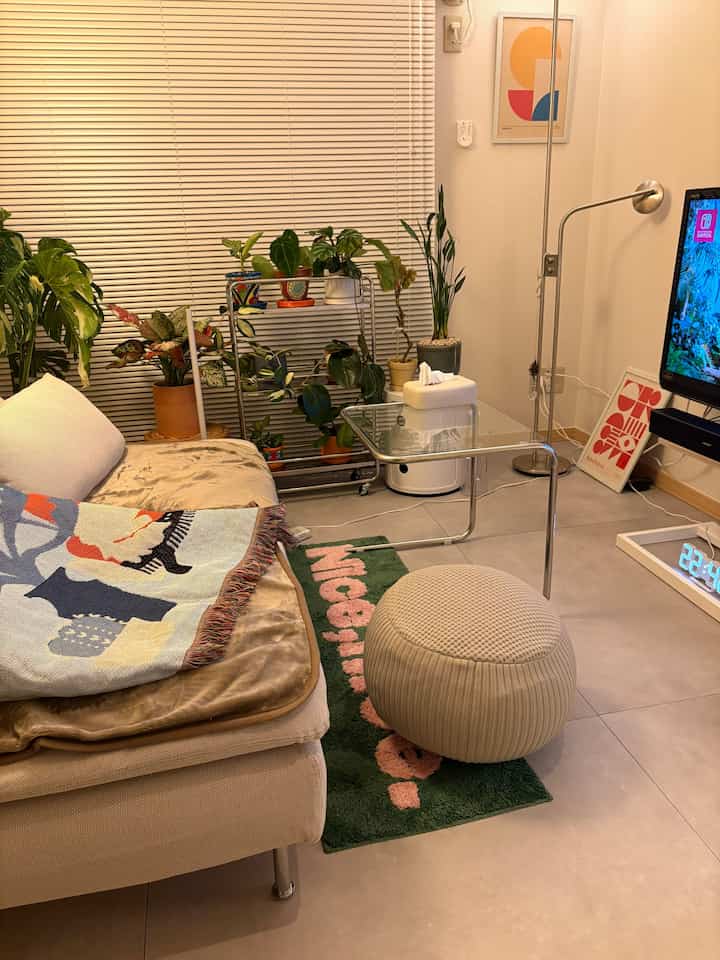 ベージュ色調のリビング、ミッドセンチュリーモダンのソファとクッション、多彩な植物が配置された雰囲気のあるインテリア