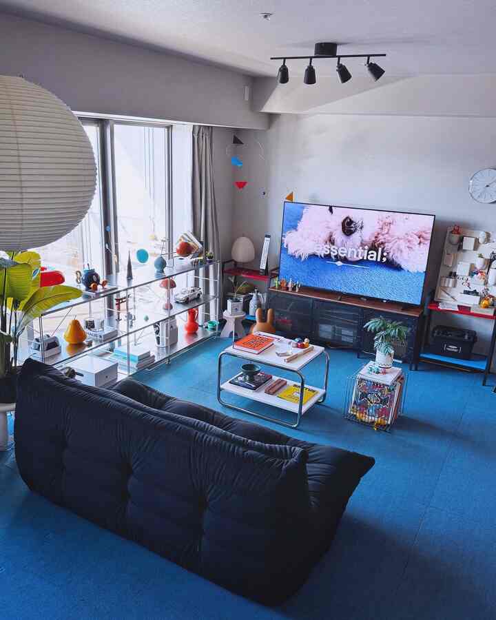 ブルーのカーペットとライトグレーの壁が調和したモダンなリビングルーム、中央にブラックのソファとテレビが配置されたホームシネマ空間