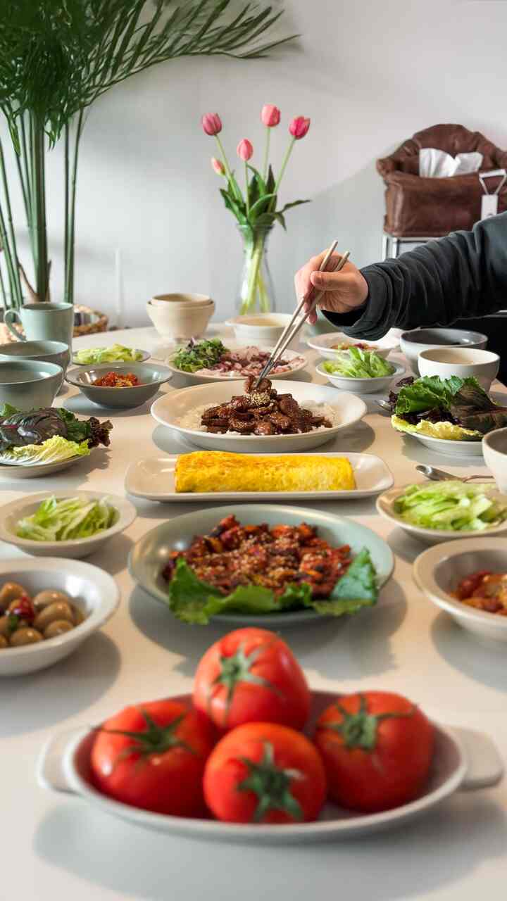 ベージュとグリーンのトーンのキッチンのダイニングテーブルにルナンセ・ミロの食器セットがホームパーティーの料理とともに美しく配置された印象的な空間