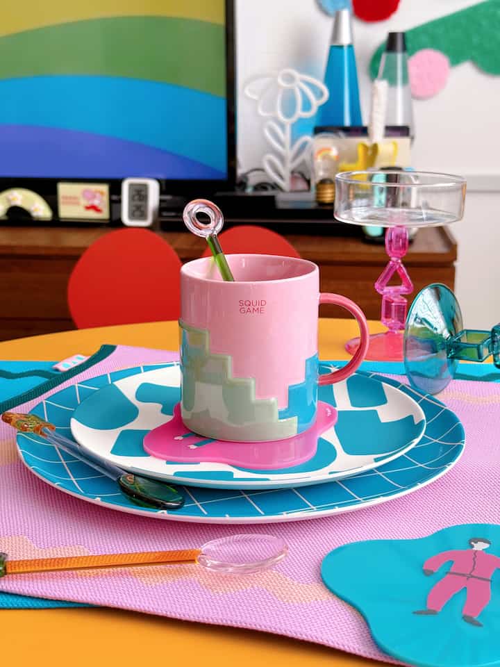 A pink and blue toned home cafe setting featuring a pink mug and blue plates on a colorful, casual table setup