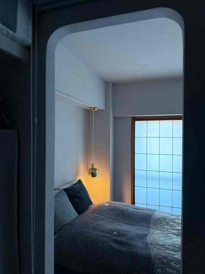 落ち着いた青色の寝室、青い寝具とゴールドのペンダントライトが配置されたミニマルなインテリア