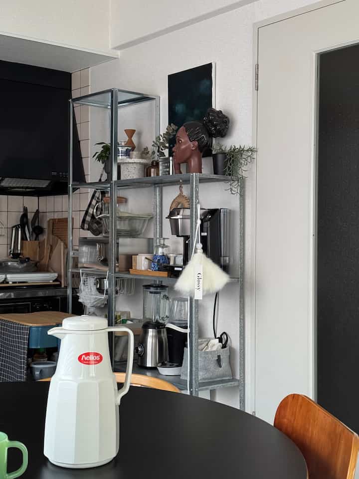 Black and white toned 1LDK kitchen featuring metal shelving with kitchenware and a round table creating a minimalist atmosphere