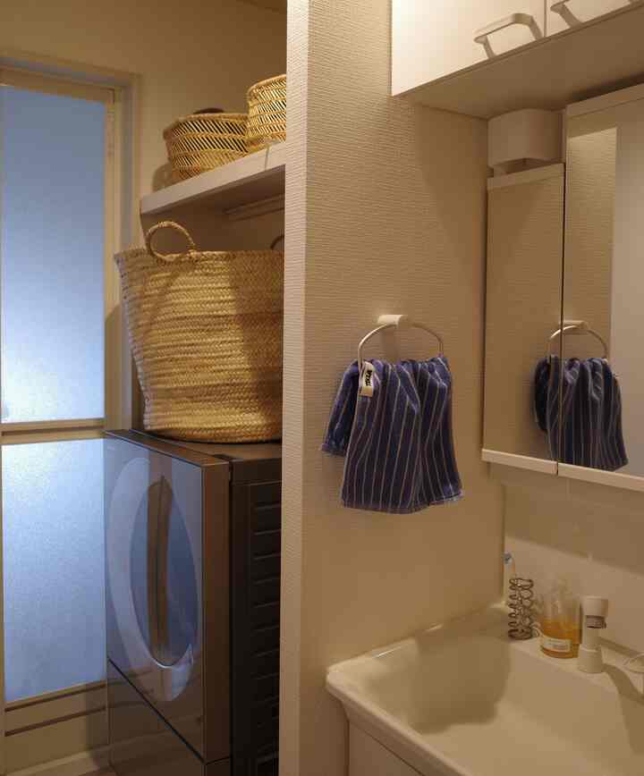 ホワイトとグレーのトーンが印象的なバスルームのコンパクトなランドリースペース、青いタオルと自然素材のバスケットが配置された清潔感のあるインテリア