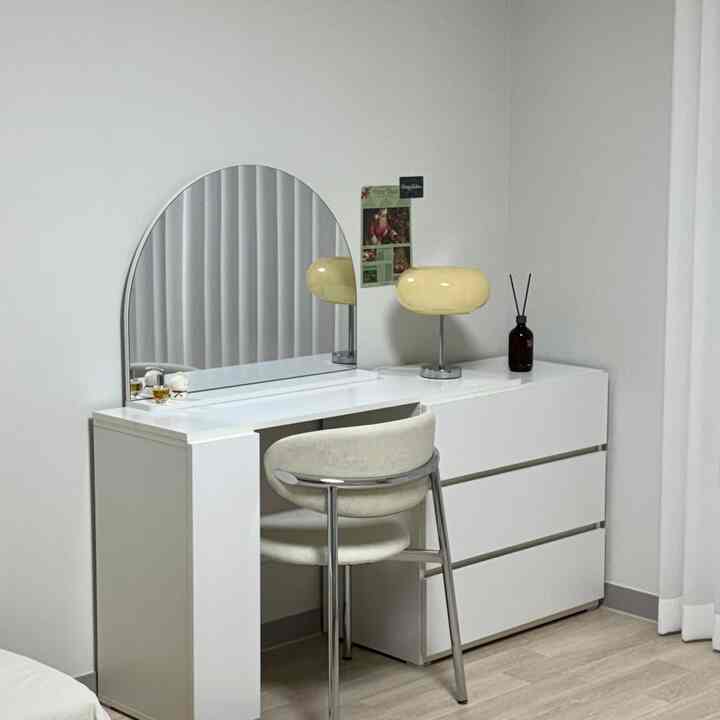 ホワイトトーンのワンルームリビング、拡張型化粧台と椅子、黄色テーブルランプが配置されたシンプルで清潔感のある空間