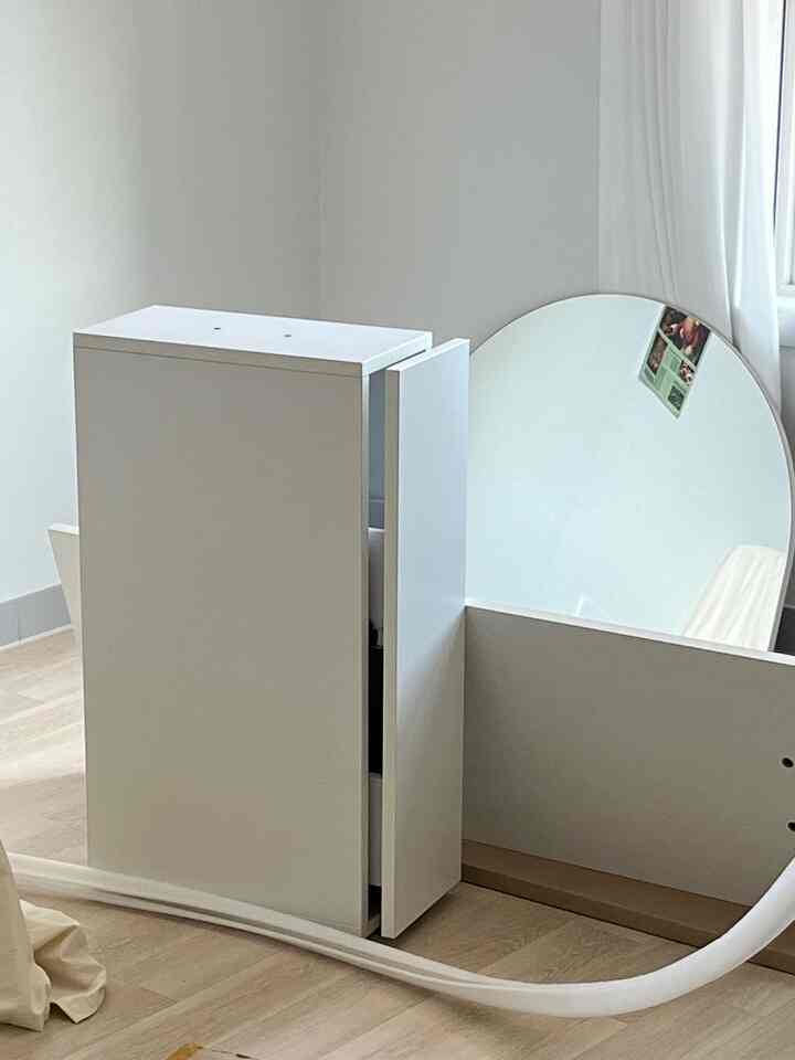 白と木目調が調和する室内空間、大型の丸い鏡と収納家具が配置された清潔感のあるインテリア