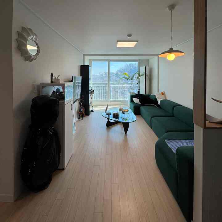 ナチュラルカラーと白い壁のリビング、グリーンのソファとガラスのテーブルが配置された印象的で落ち着いた空間