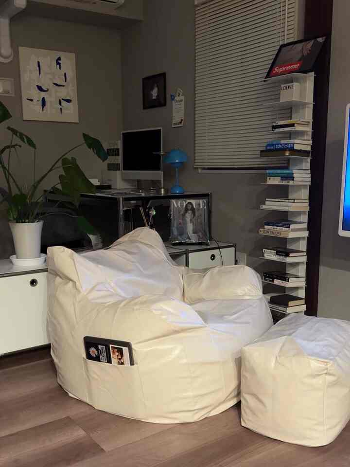 クリーム色のナチュラルトーンのリビング、中央に快適なビーズクッションソファとスツールがあり、モダンなホームオフィスが配置された印象的な空間