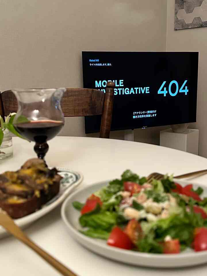 白い円形のダイニングテーブルと茶色い椅子が置かれたリビング、テーブルにサラダ、ワイングラス、パンが並び、雰囲気のあるおうちカフェ空間