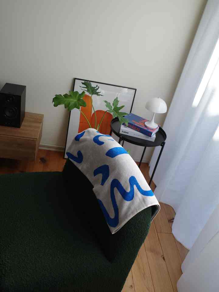 ナチュラルトーンのベージュの壁の空間、青い模様のタオルとポスター、植物、サイドテーブルが配置された落ち着いたインテリア