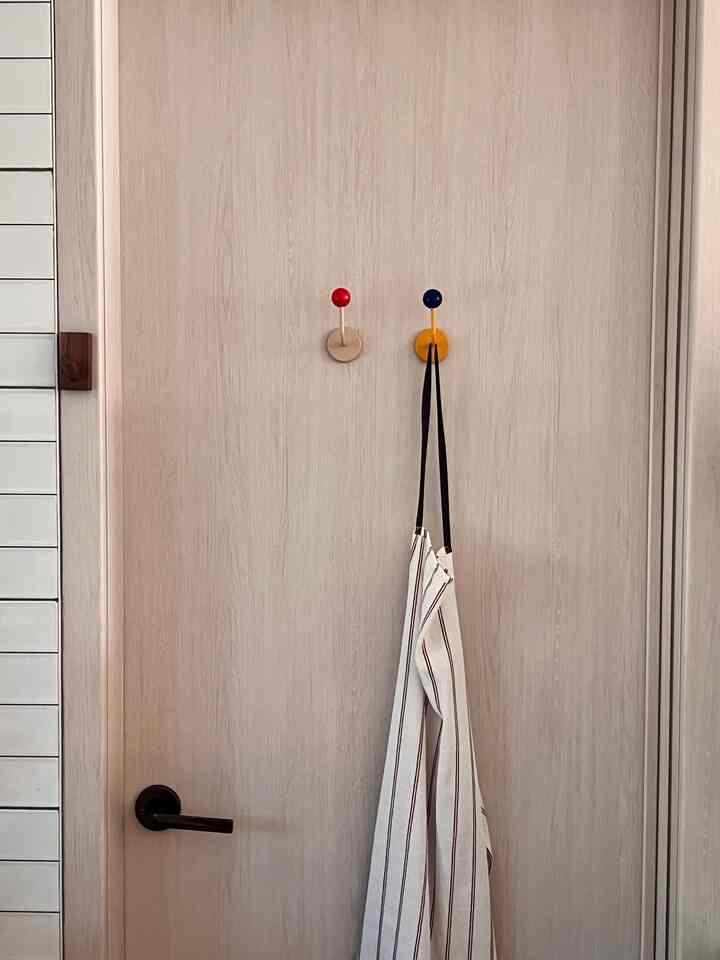 Natural tone kitchen door with red and navy hooks holding an apron