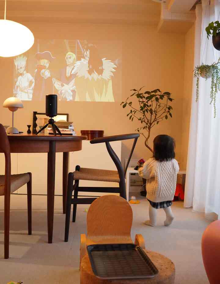 ベージュ色の床とナチュラルモダンなダイニングルーム、歩く幼児とアニメが壁に投影されているリビング空間