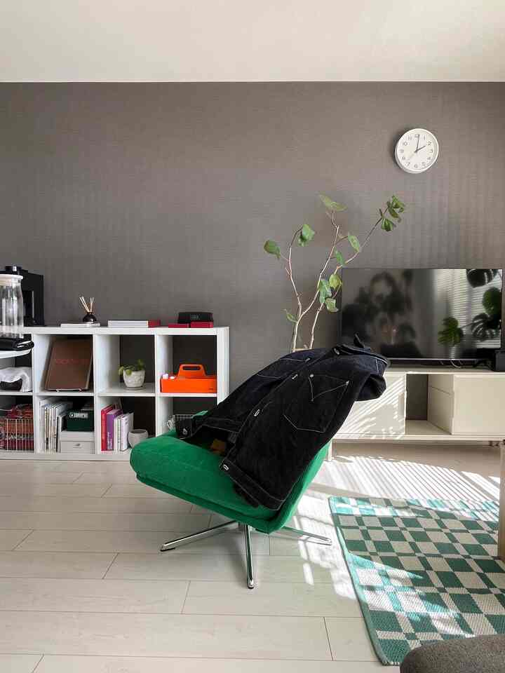 白い壁と床、緑のアームチェアと市松模様のラグが調和するミッドセンチュリーモダンのリビング