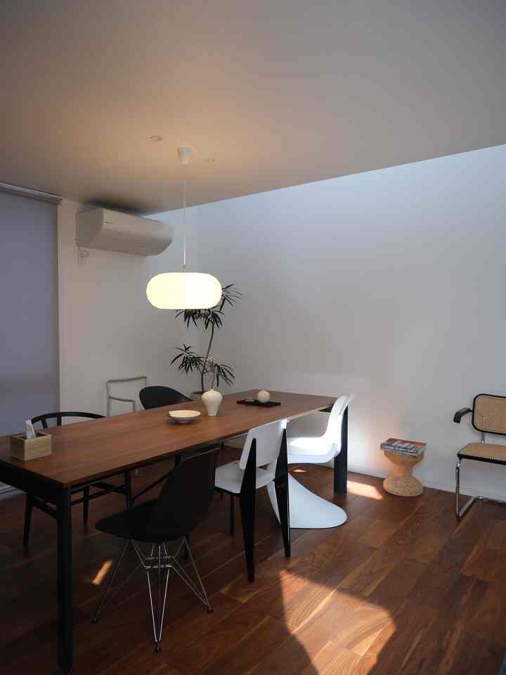 White and brown toned living room featuring a central wooden dining table and various dining chairs with a simple, natural atmosphere