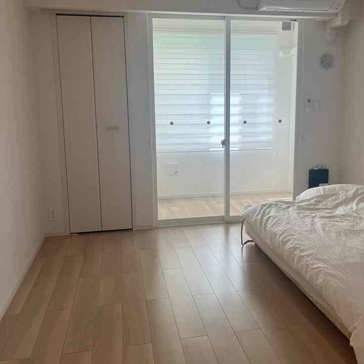 Bright white and wood tone 1K bedroom featuring a bed and veranda door, presenting a clean, compact living space