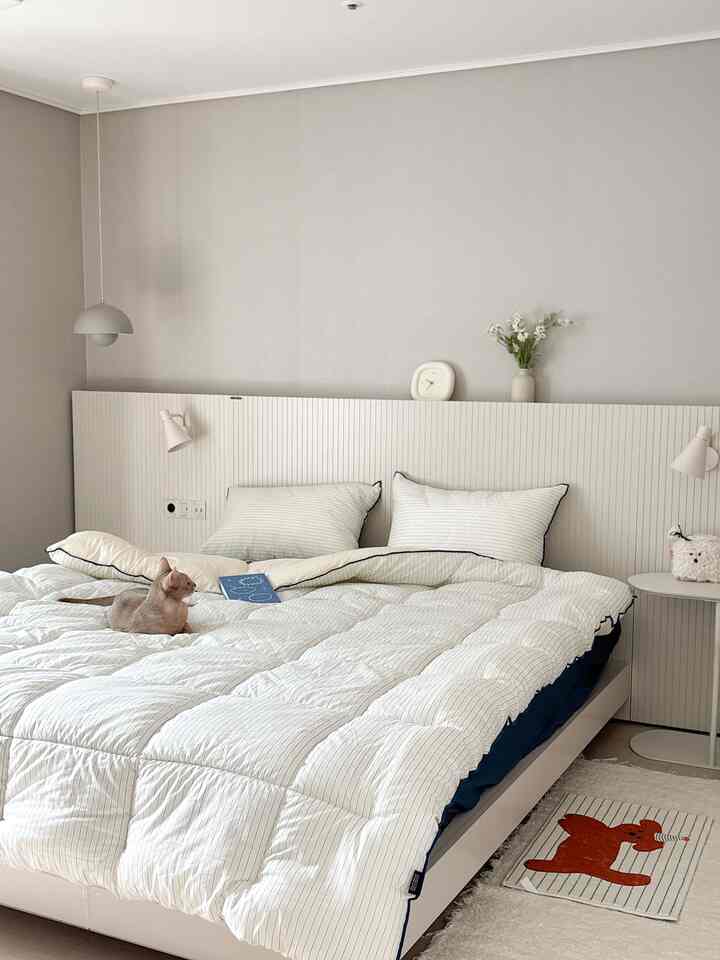 White and beige toned bedroom featuring a large central bed with a cat, showcasing a natural modern style space