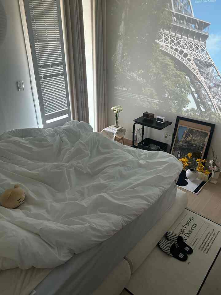 A cozy bedroom in white and wood tones featuring a large king-size bed and a projector display