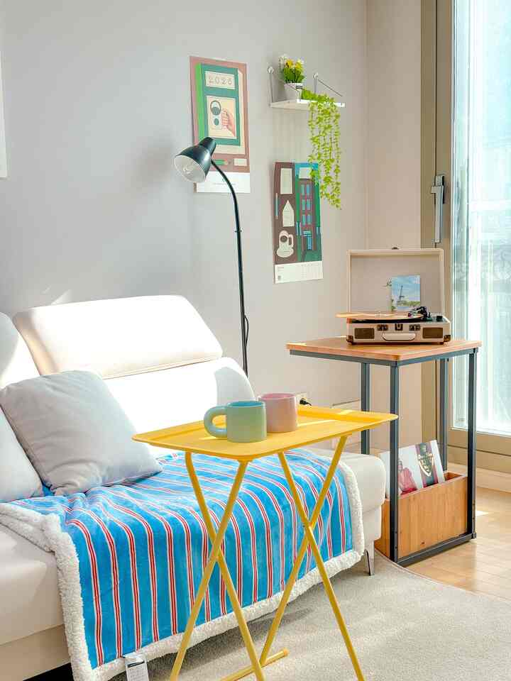 Bright living room with white and wood tones, featuring a sofa draped with a blue striped blanket and a yellow folding table as focal points