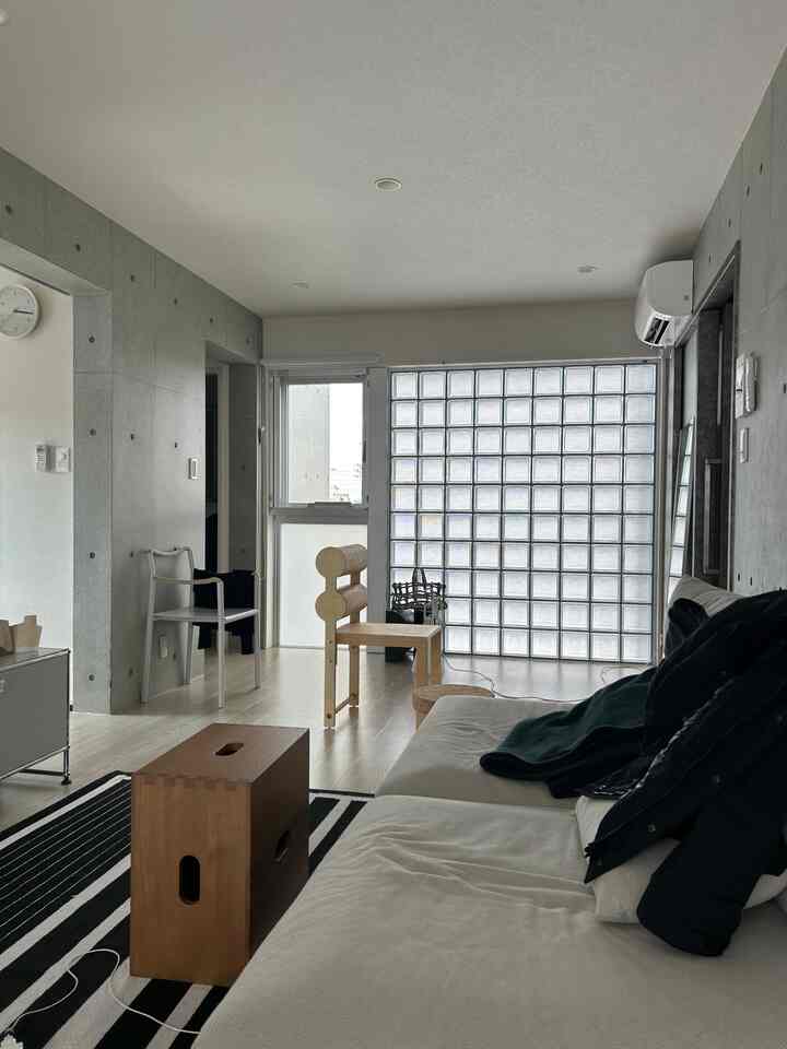 ホワイトとグレーのトーンのリビング、自然光が差し込むミニマルな木製家具が配置されたモダンな空間