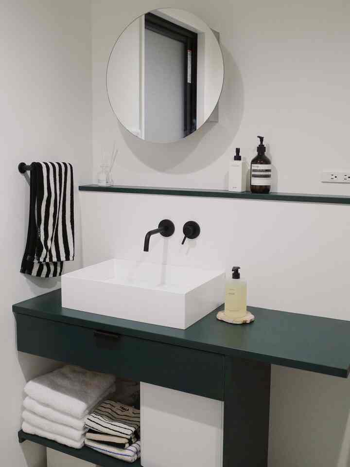 ホワイトとダークグリーンのトーンのバスルーム、清潔な洗面台と棚に整頓されたタオルが配置されたモダンな空間